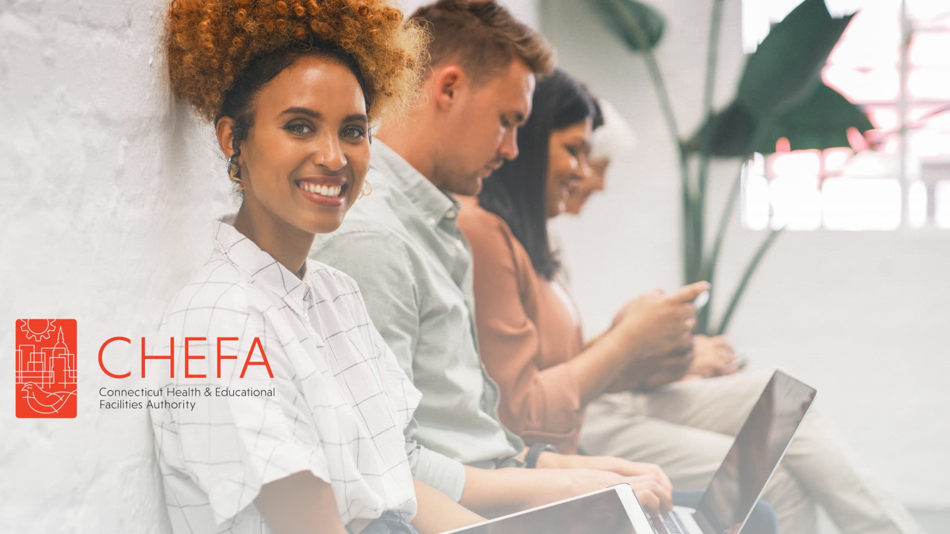 People sitting against wall, closest one smiling at the user.