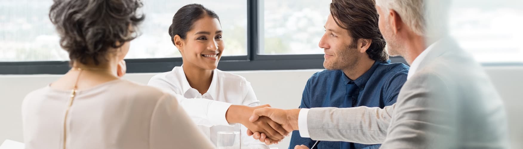 A group of employees collaborate and shake hands in the conference room.