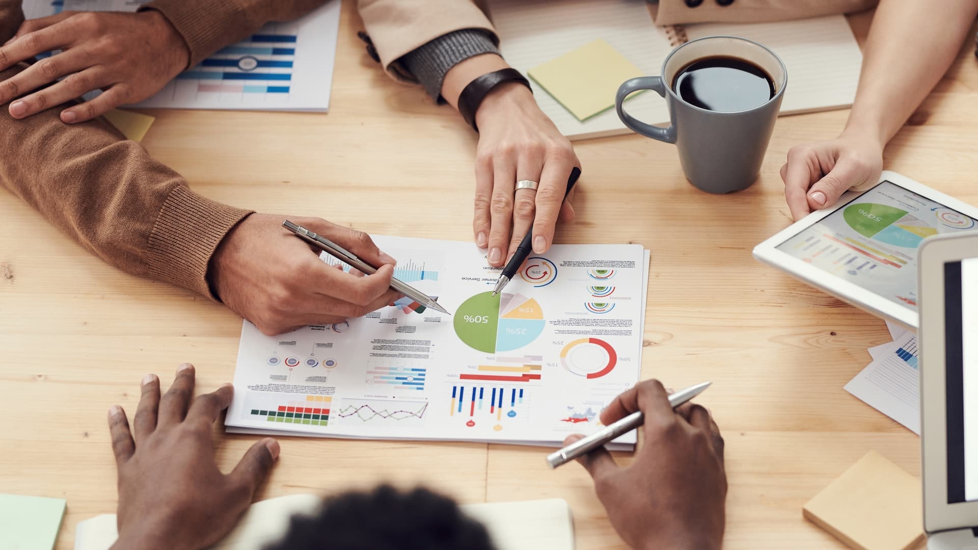 hands holding pens pointing to a report with graphics