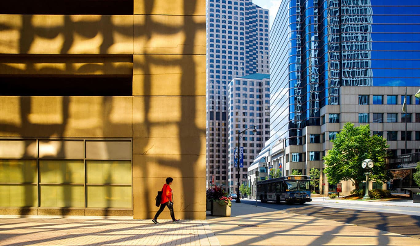 A woman walks across the street amongst large buildings in the city
