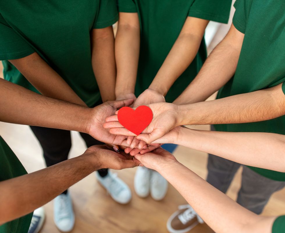 Circle of hands coming together to hold a paper heart