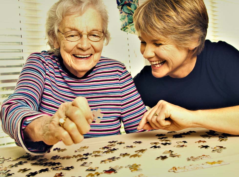 An elderly woman smiles while working with puzzle pieces