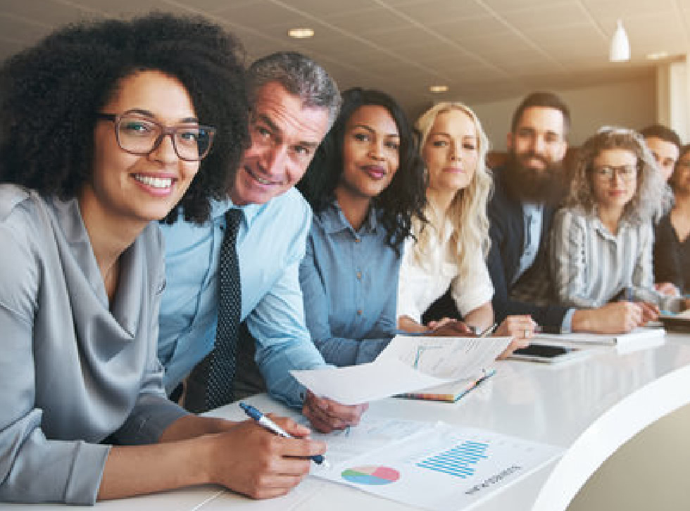 A group of smiling employees lean on a curved table.