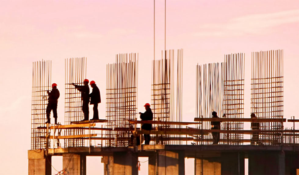 Iron workers at sunset on the top of a building under construction.