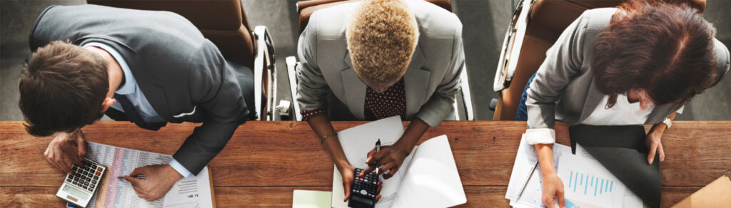 Three employees work on their presentation papers at a desk.